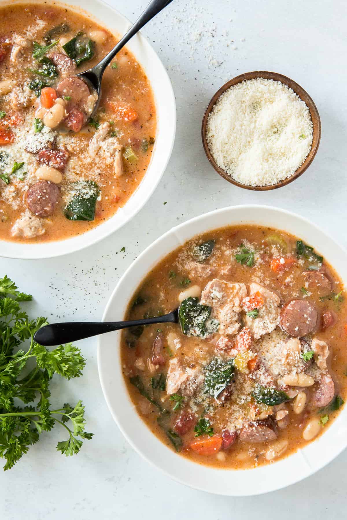 A top down shot of two bowls filled with chicken and sausage stew topped with grated Parmesan cheese.