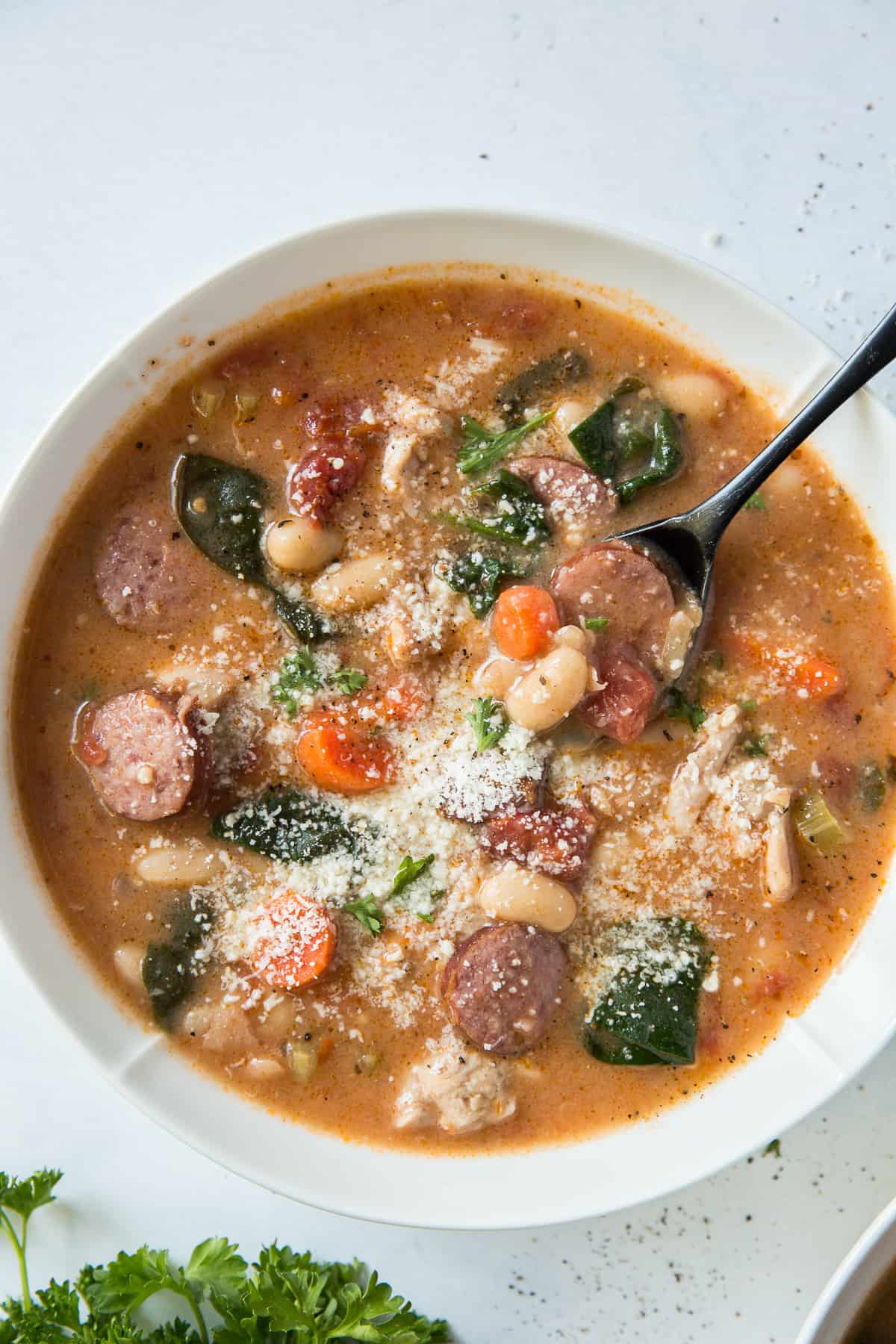 A top down close up of a bowl of chicken and sausage stew with a spoon.