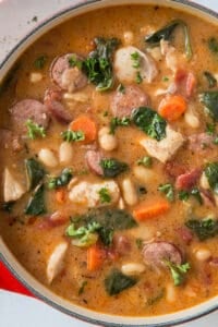 A top down shot of a pot filled with chicken and sausage stew with white beans and spinach.