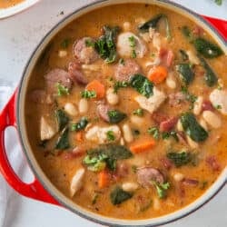 A top down shot of a pot filled with chicken and sausage stew with white beans and spinach.