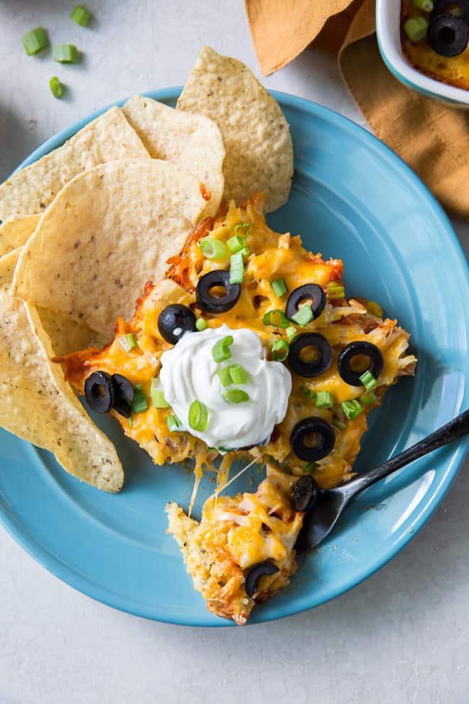 A slice of tamale casserole on a blue plate topped with sour cream.