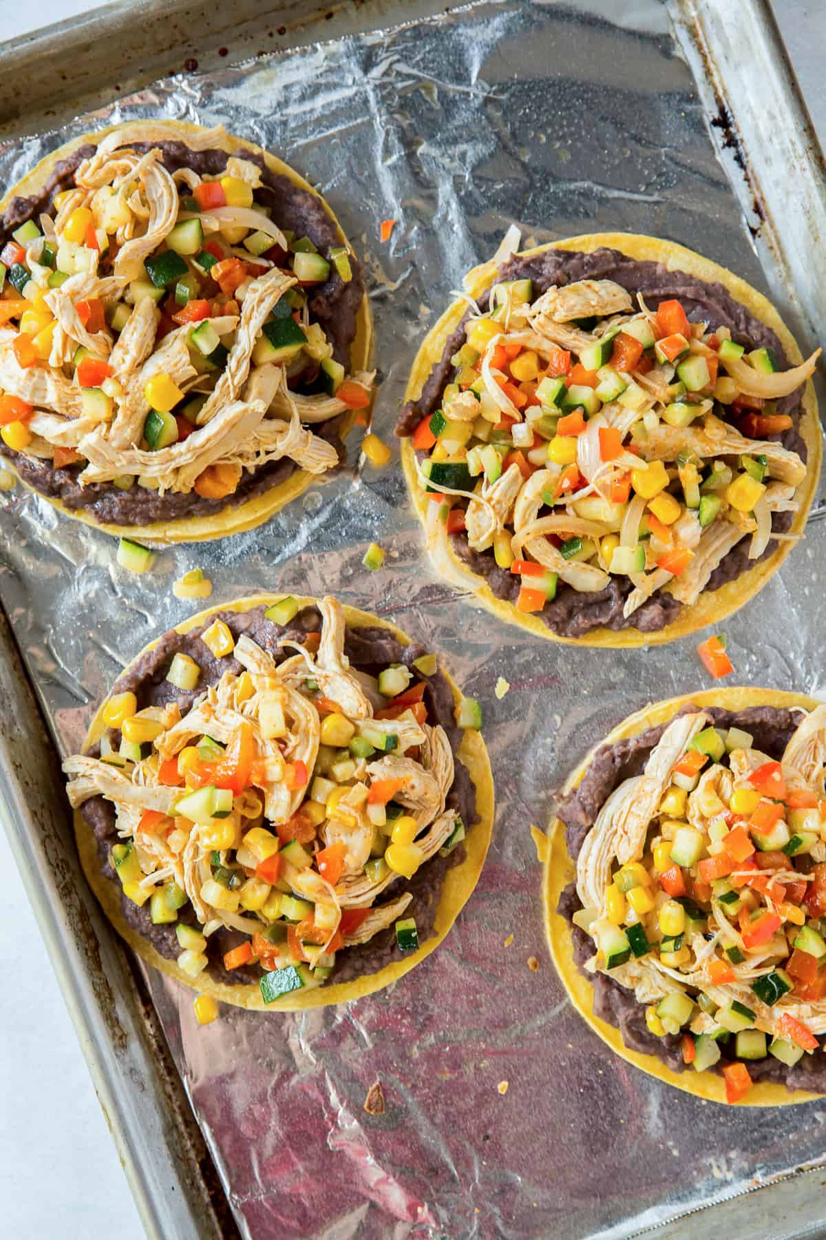 Tostadas on a baking sheet topped with chicken and vegetables.