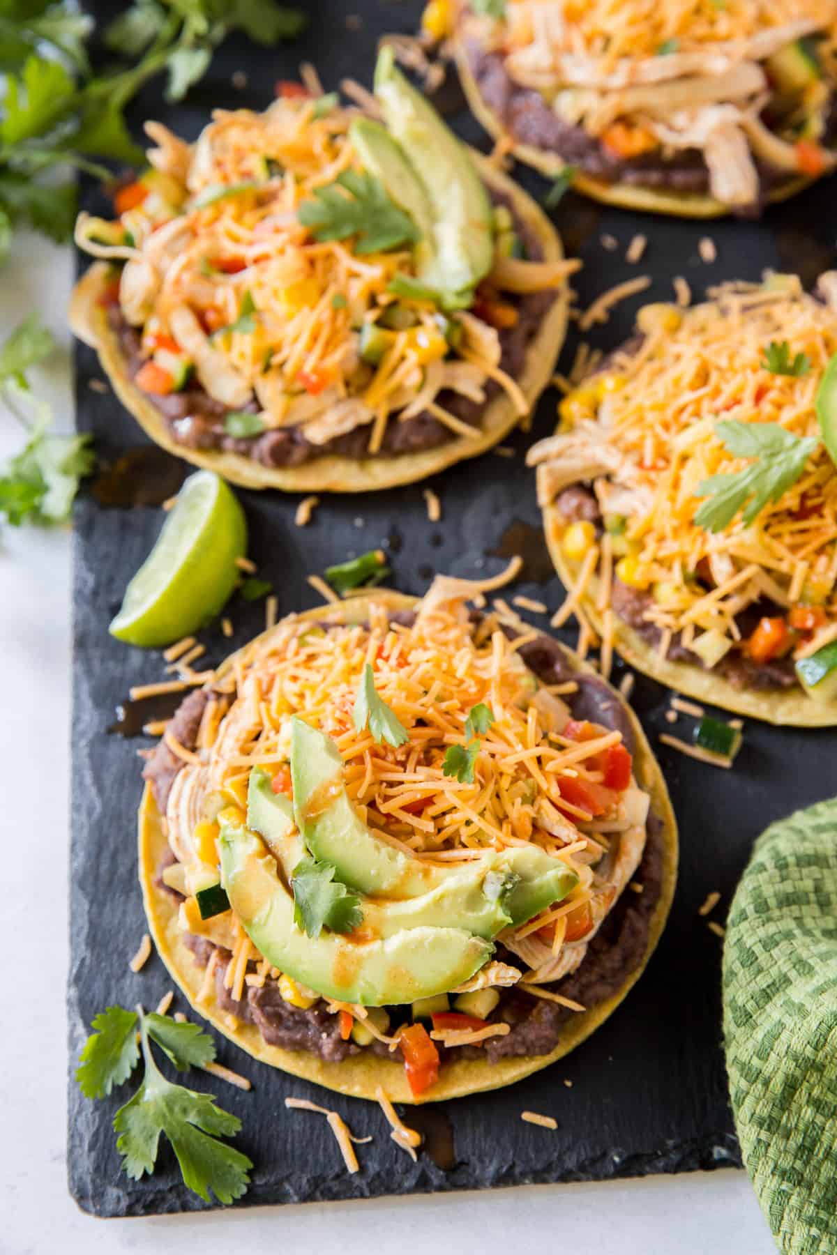 Tostadas topped with shredded cheddar cheese and sliced avocado.