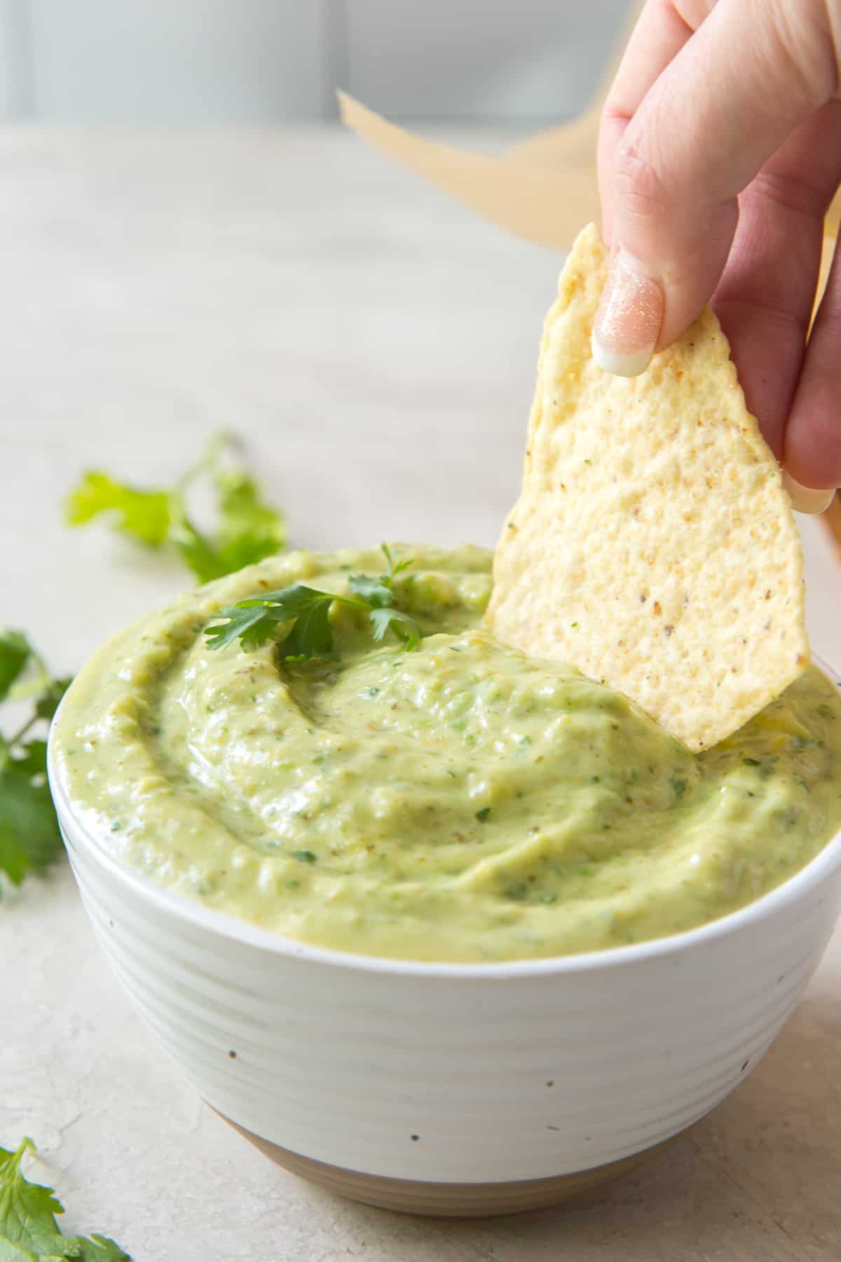 A hand dipping a chip into tomatillo avocado salsa.