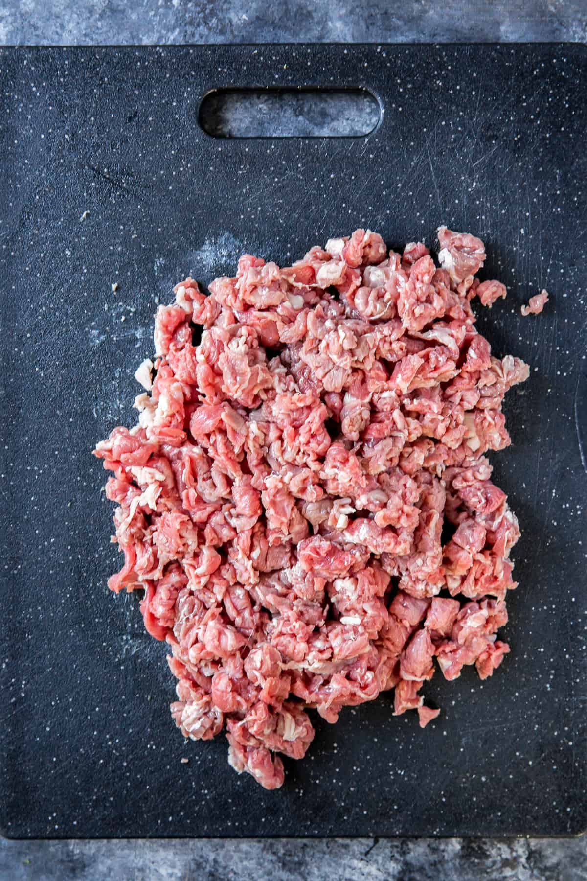 Chopped raw steak on a black cutting board.