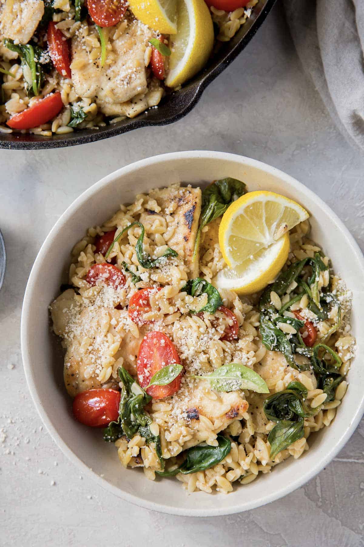 Lemon chicken with orzo topped with lemon slices and parmesan in a white bowl.