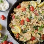A skillet filled with orzo, chicken, grape tomatoes, and slices of lemon.