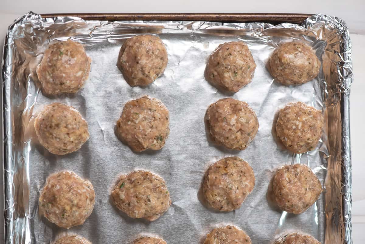 A top down shot of chicken meatballs on a foil lined baking sheet.