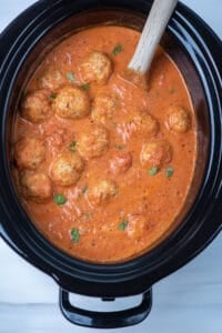 A slow cooker insert filled with marinara sauce and meatballs.