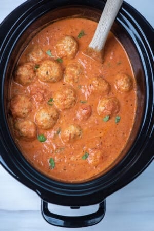 A slow cooker insert filled with marinara sauce and meatballs.