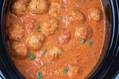 A slow cooker insert filled with marinara sauce and meatballs.