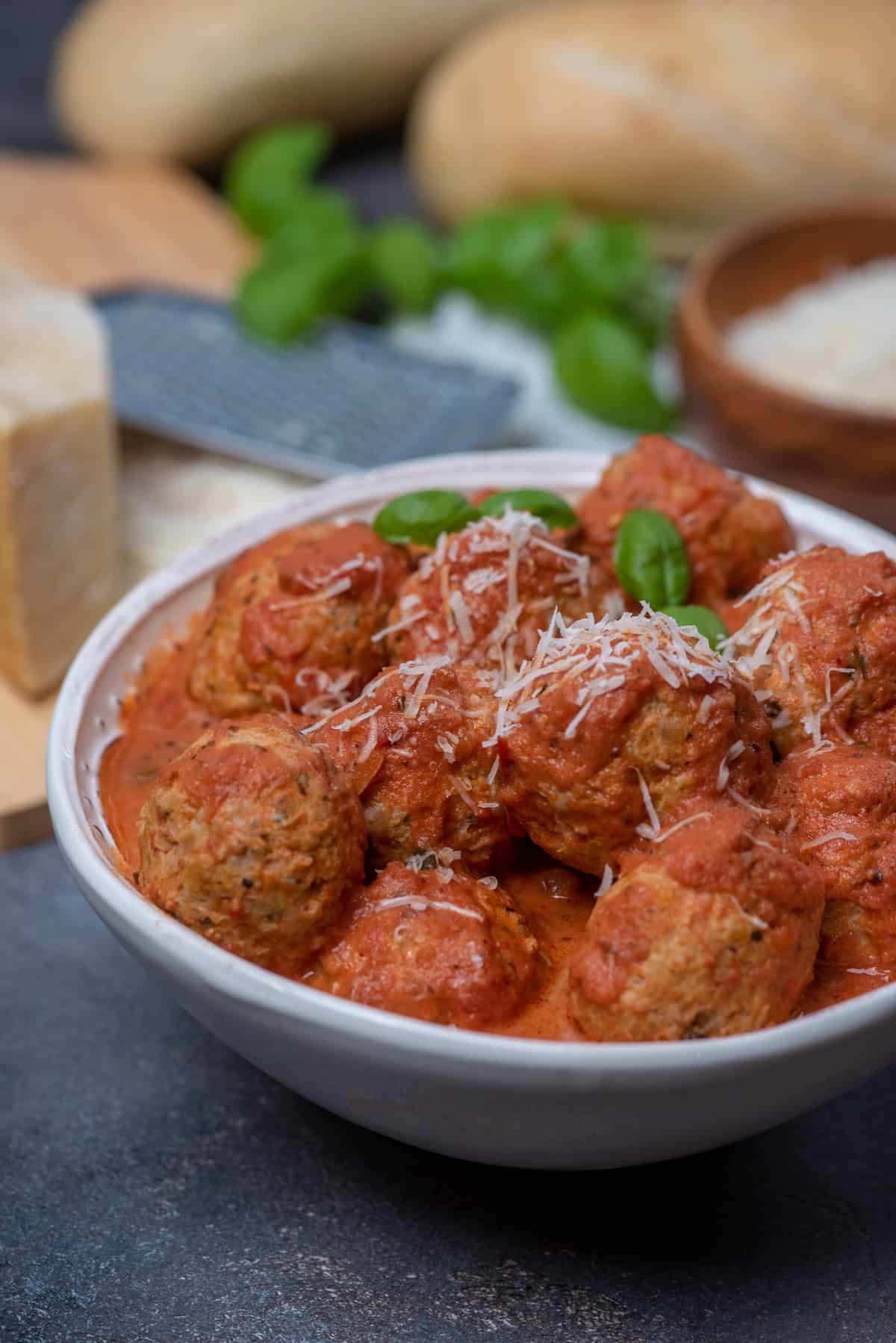 Chicken parmesan meatballs topped with parmesan cheese in a white bowl.