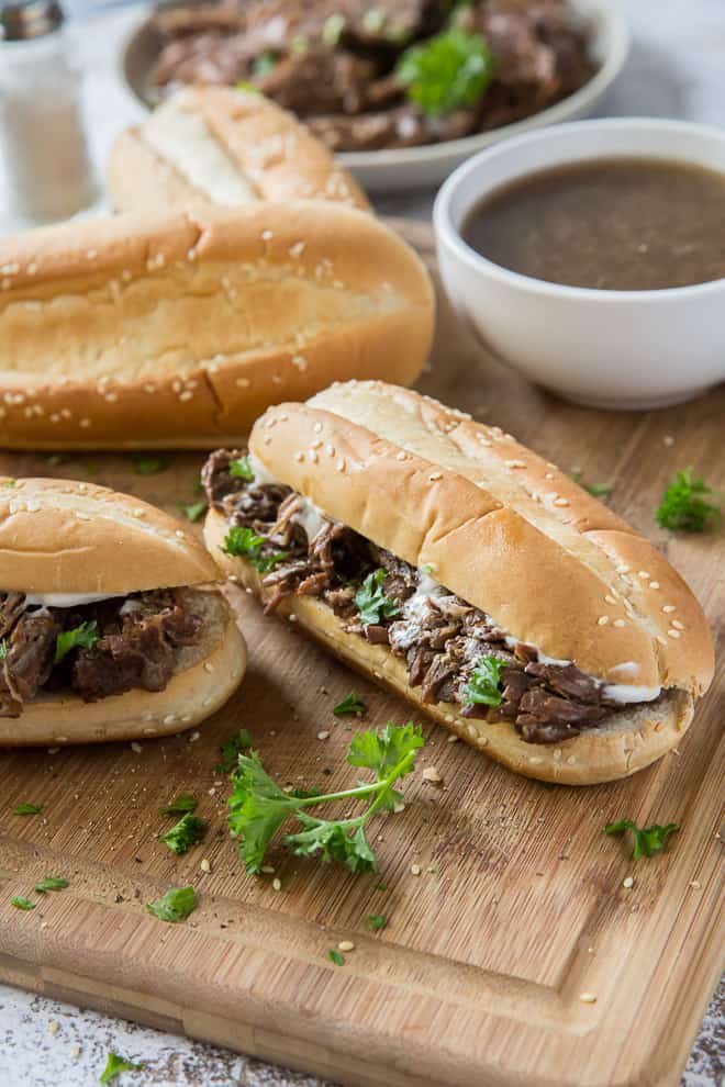 French Dip Sandwiches on a cutting board with bits of parsley around it.