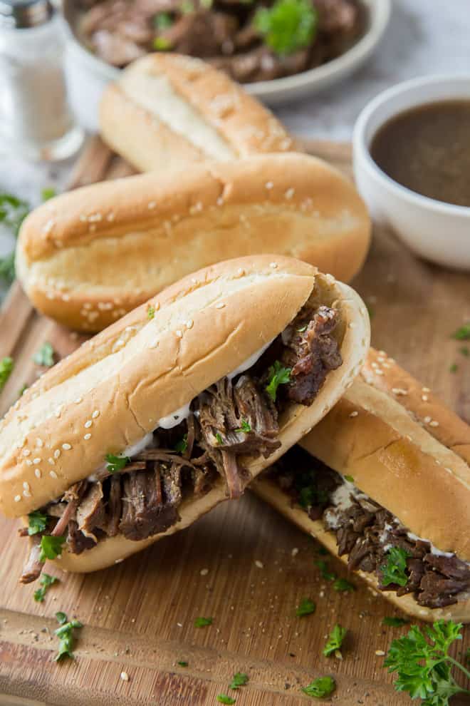 Shredded beef on hoagie rolls stacked on a cutting board.