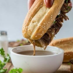 A sandwich being dipped into a small bowl of au jus.