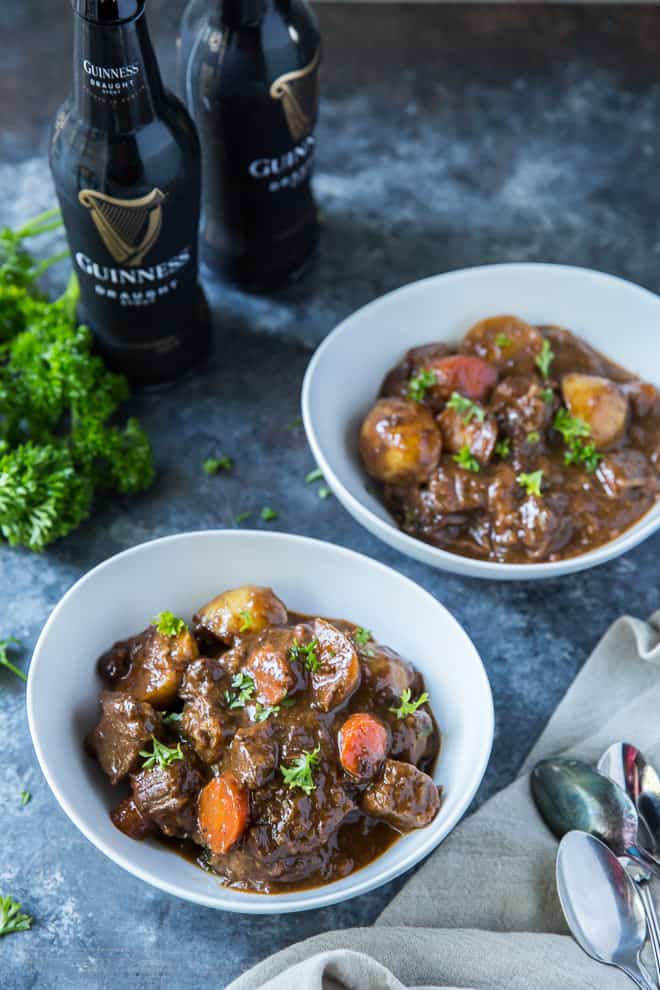 Two white serving bowls of Irish Beef Stew with two bottles of Guinness Draught behind them.