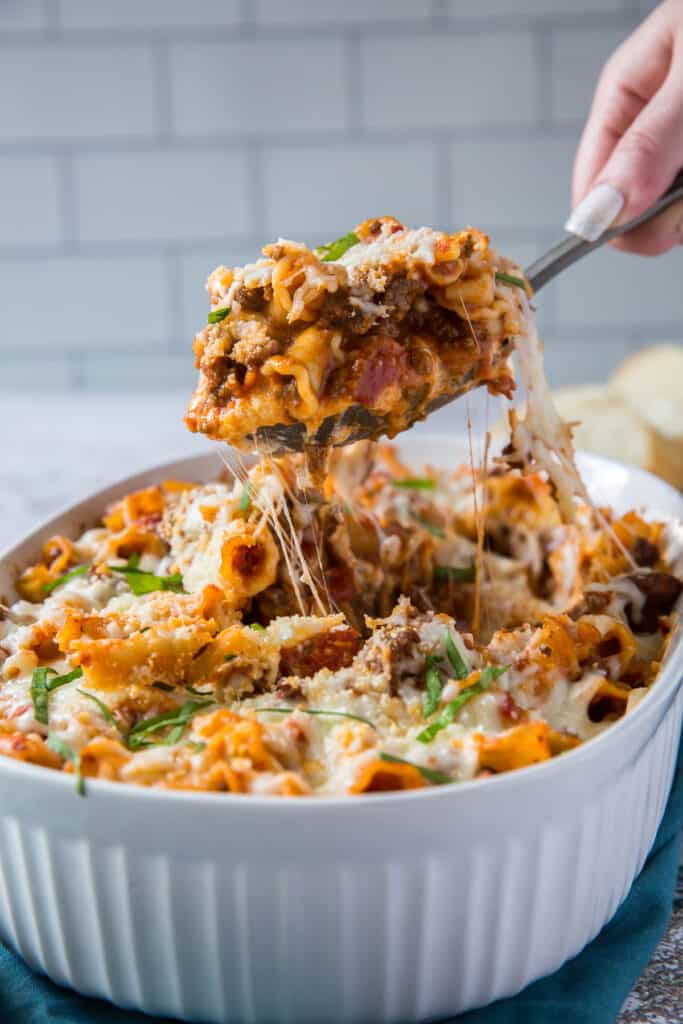 A spoon lifts a scoop of the lasagna casserole from the dish.