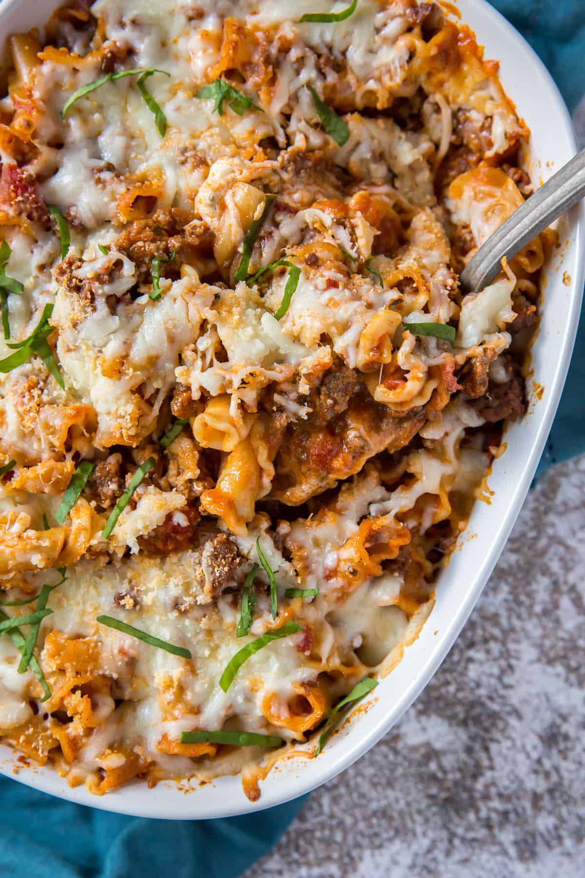 A close up image of a spoon digging into the easy pasta casserole in a white baking dish.