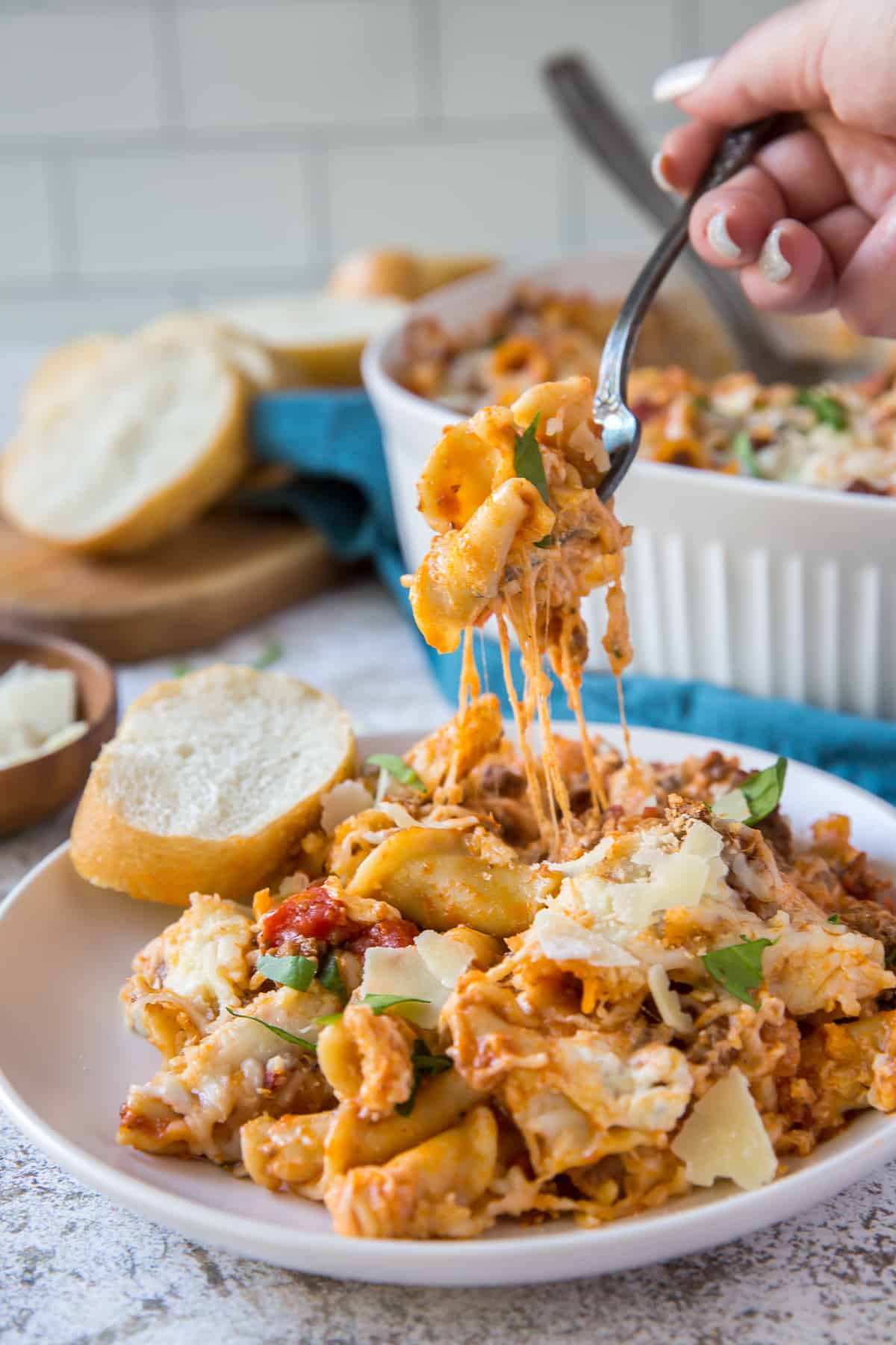 A fork lifts up a bite full of the Lazy Lasagna Casserole from a white serving plate.