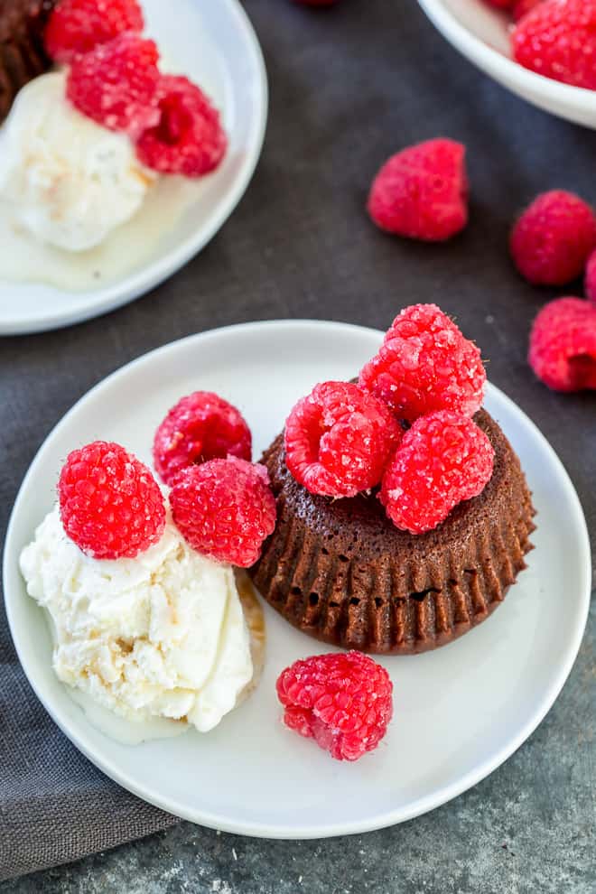 A lava cake topped with sugared raspberries and served with vanilla ice cream on a white serving plate.