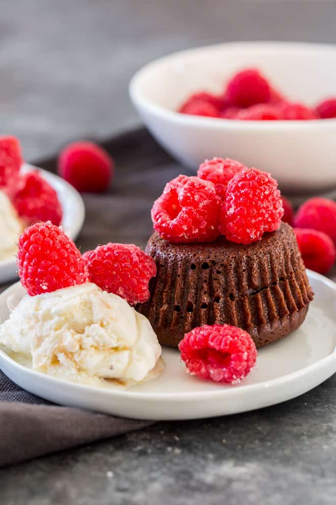 A Molten Chocolate Cake topped with sugared raspberries and served with vanilla ice cream on a white serving plate.