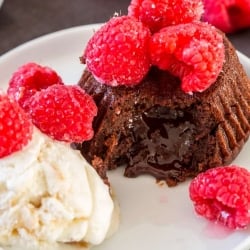 A chocolate cake topped with raspberries with a scoop of ice cream.