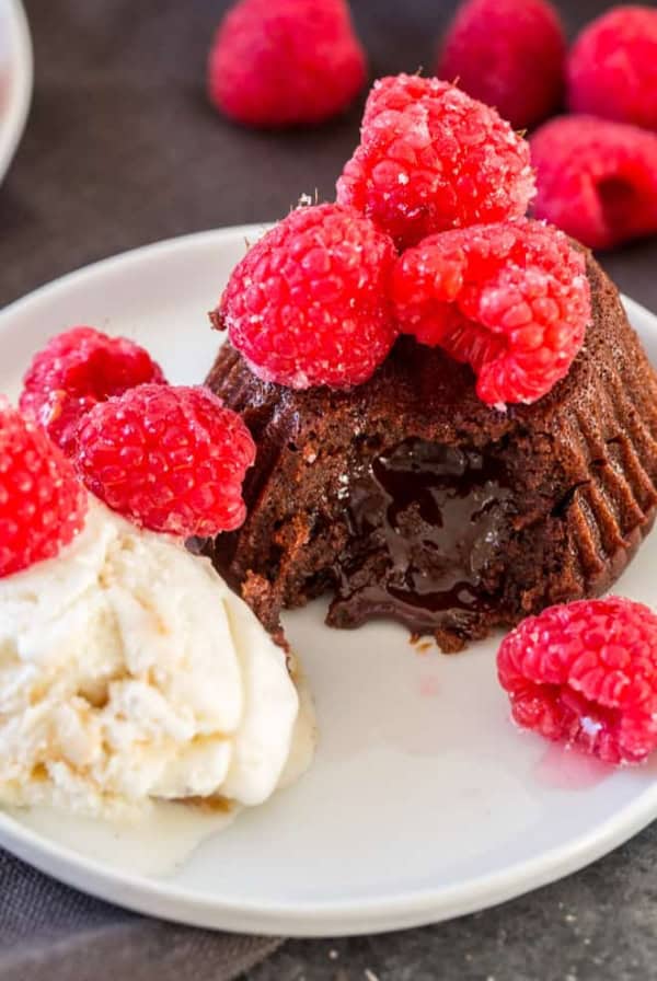 A chocolate cake topped with raspberries with a scoop of ice cream.