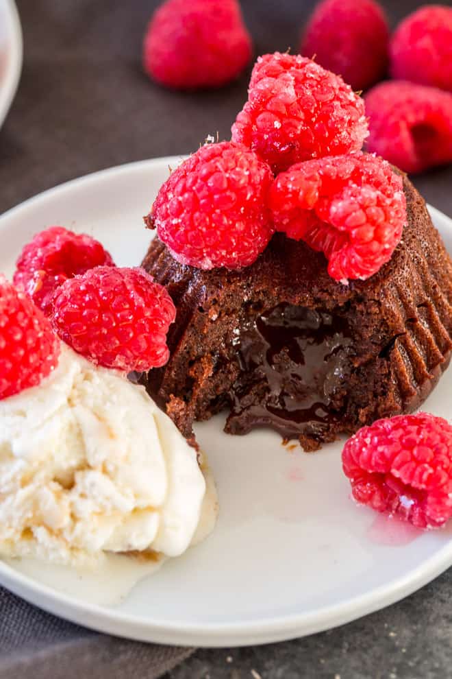 A chocolate cake topped with raspberries with a scoop of ice cream.