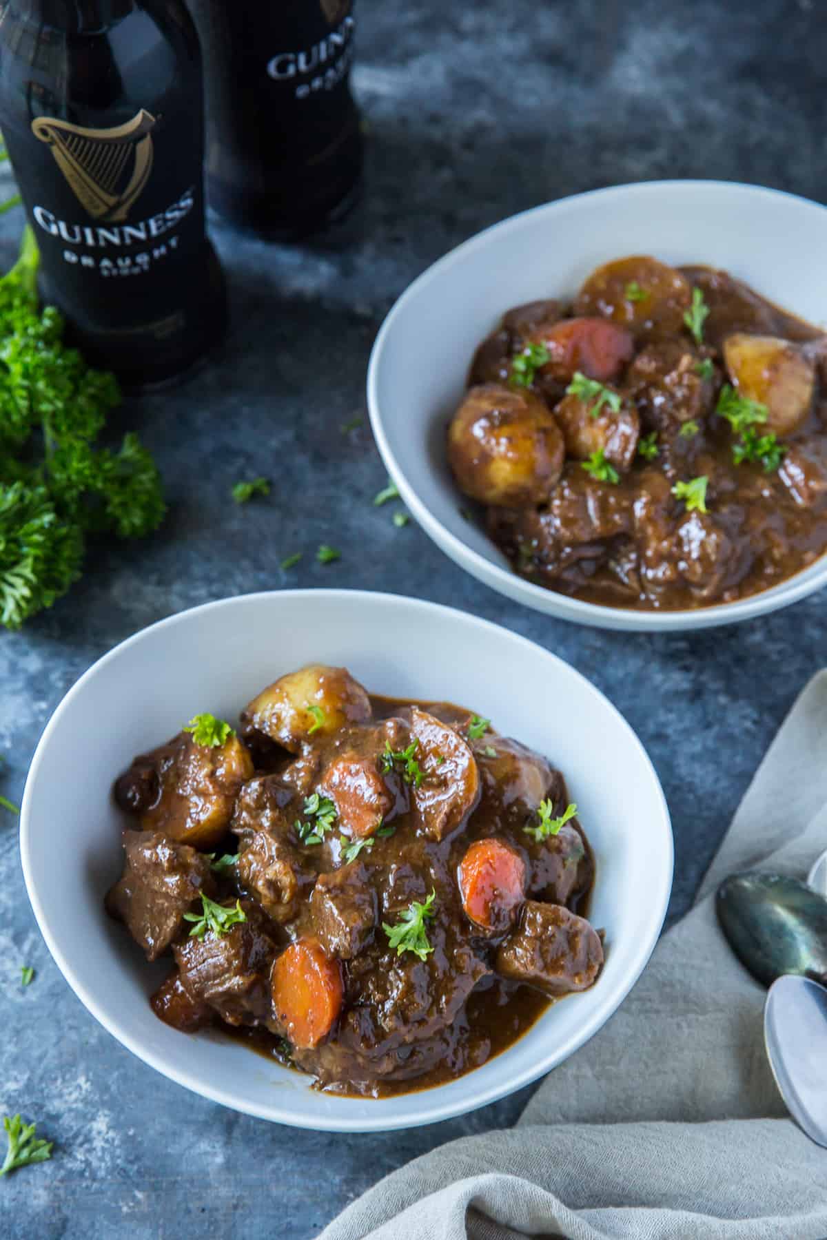 Two bowls of Irish beef stew next to two bottles of Guinness beer.
