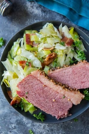 Corned beef with sauteed cabbage on a black plate.