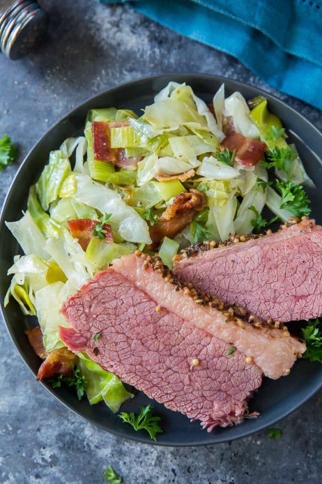 A serving of cabbage with leeks and bacon on a plate with slices of corned beef.