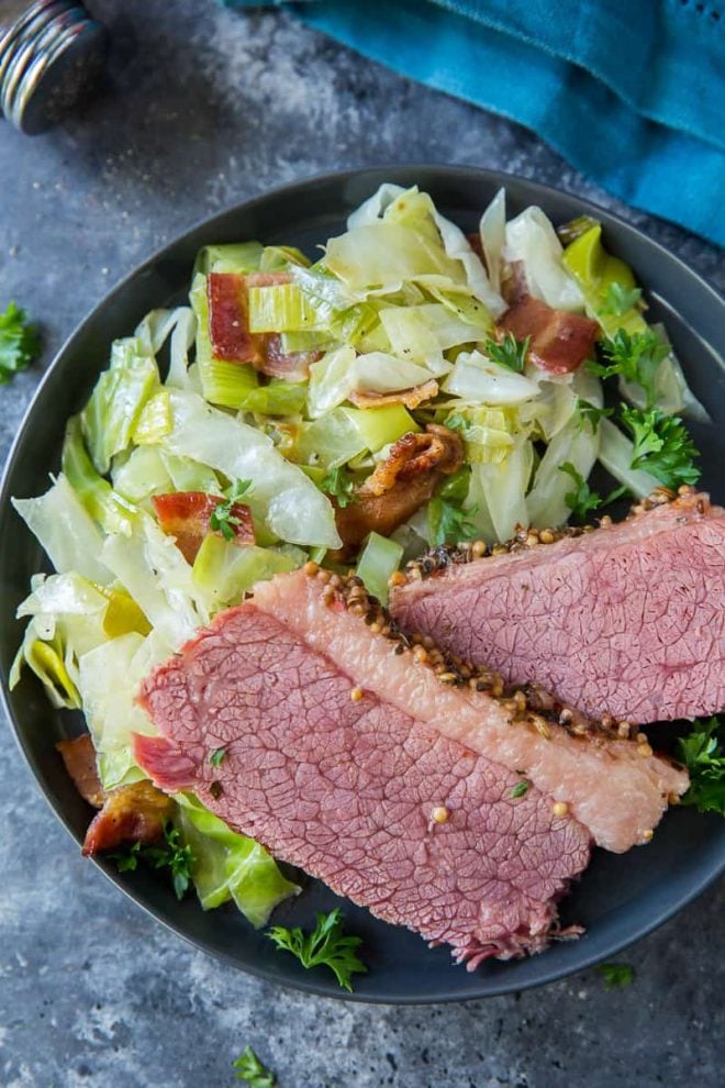 Corned beef with sauteed cabbage on a black plate.