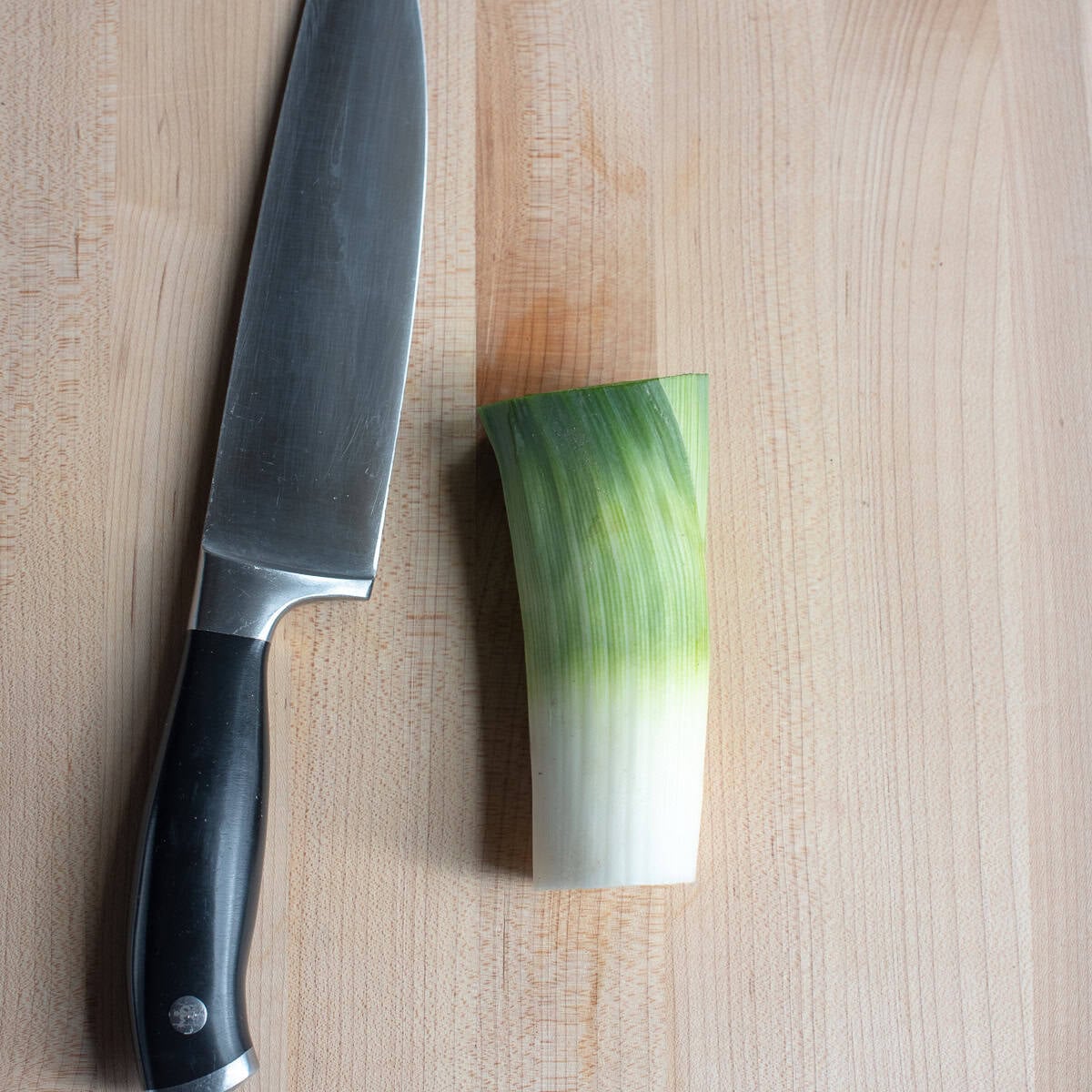 A trimmed leek on a cutting board with a knife.