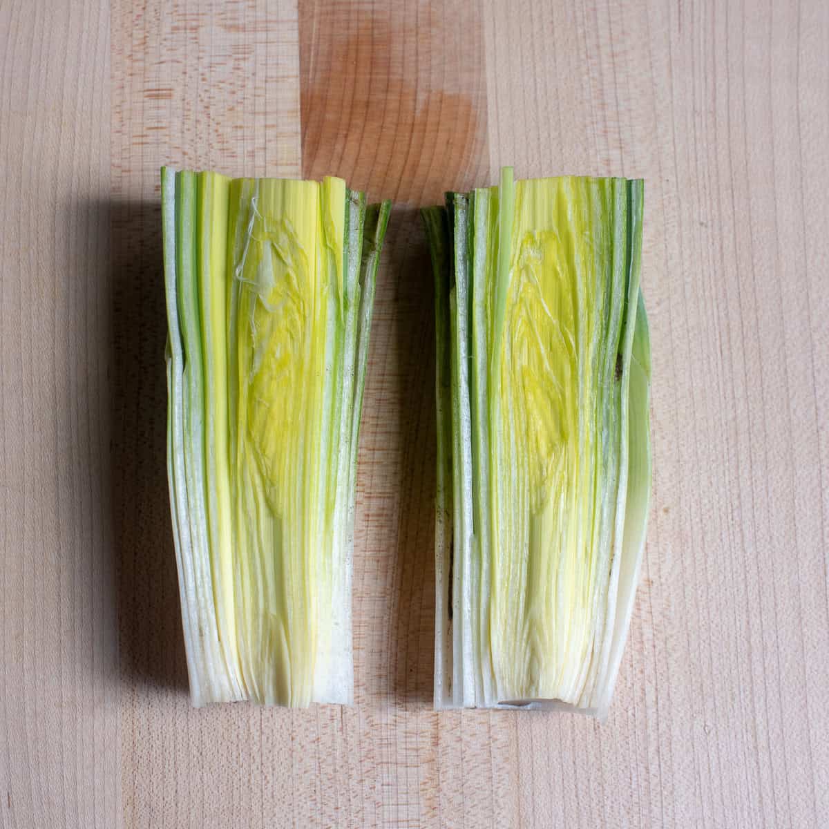 A leek sliced in half on a cutting board.