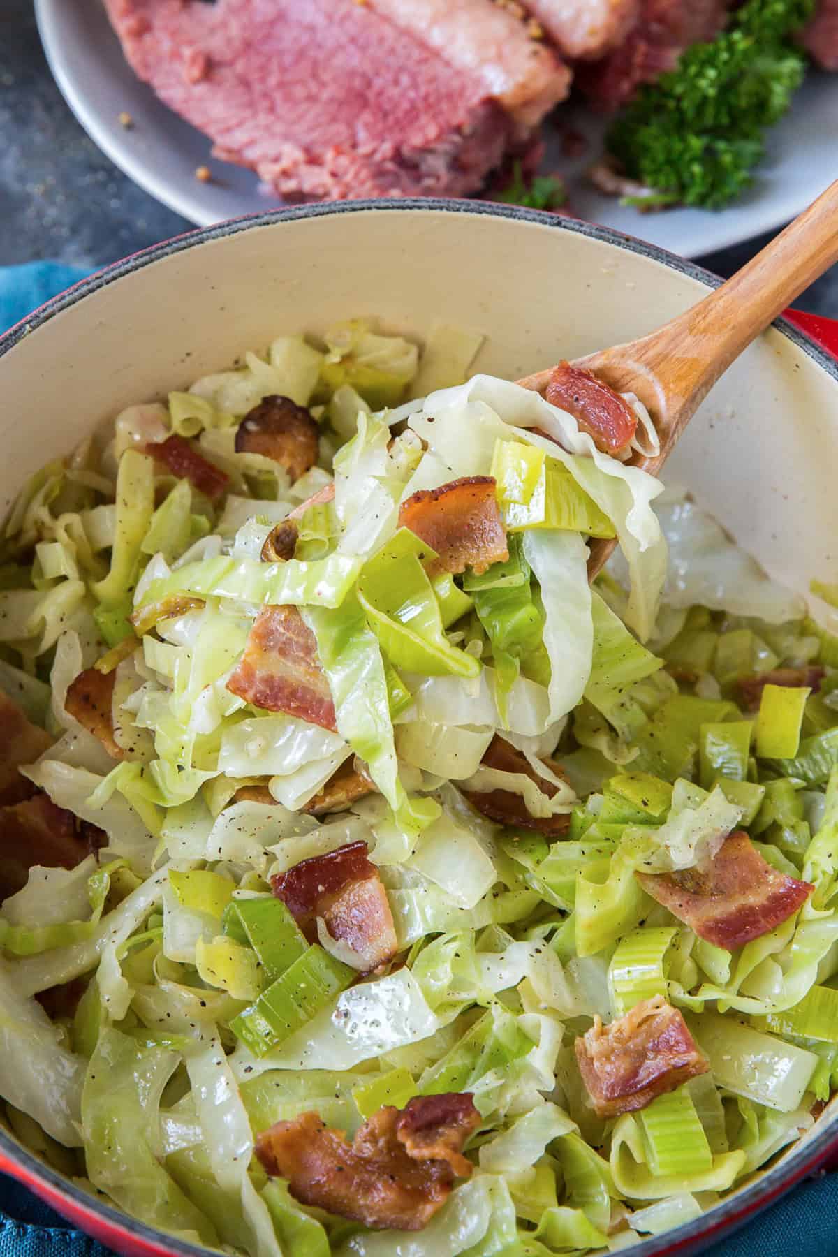 A wooden spoon scooping sauteed leeks from a Dutch oven.