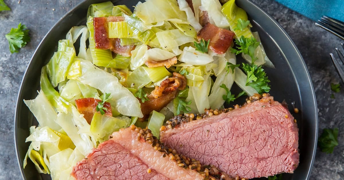 Sauteed cabbage with leeks and bacon on a blue plate with corned beef.