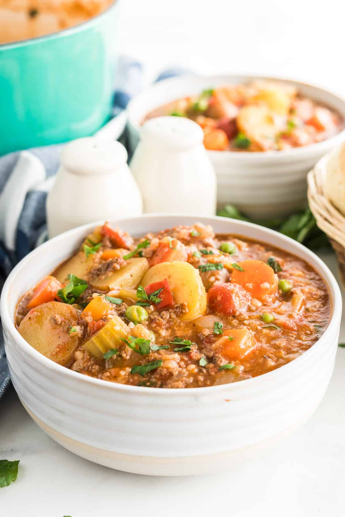 A white serving bowl filled with Hamburger Stew with salt and pepper shakers in the background.