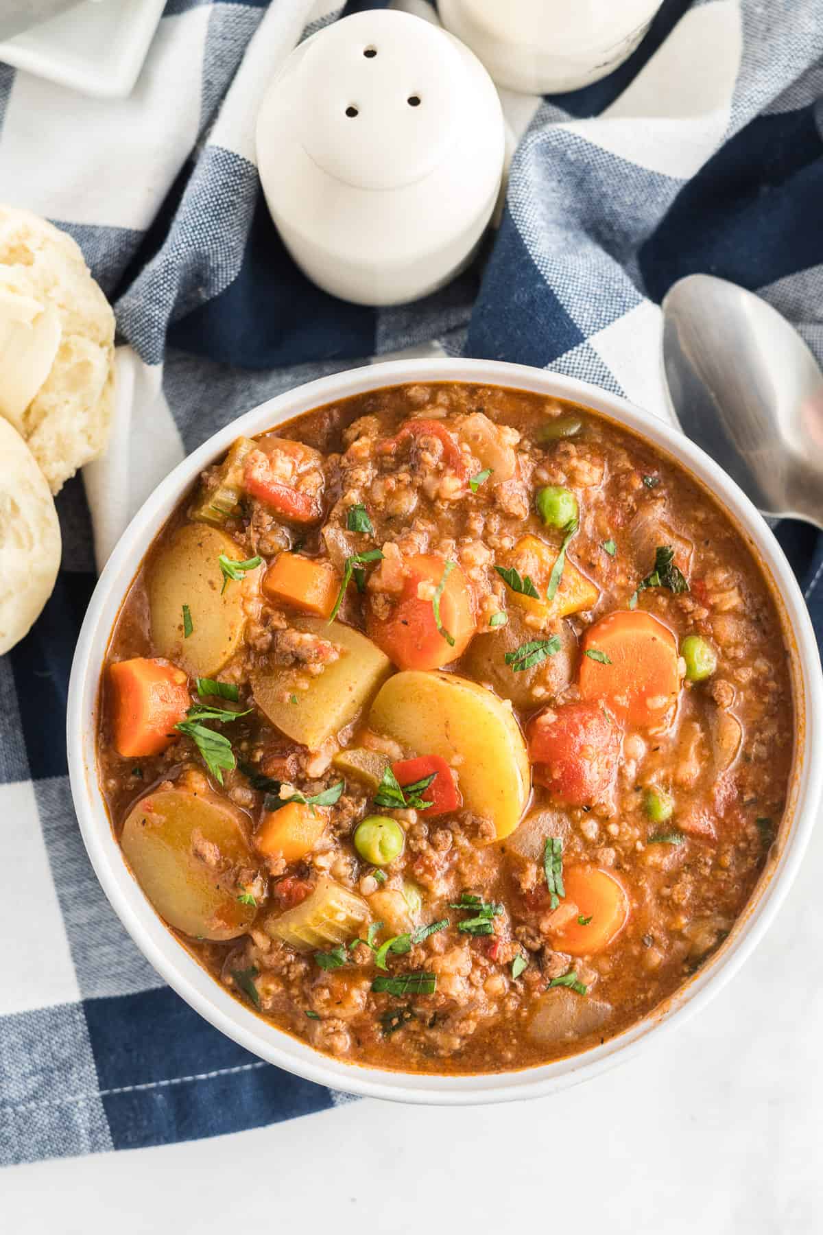 A bowl full of Hamburger Stew on a blue plaid napkin shot from over the top.