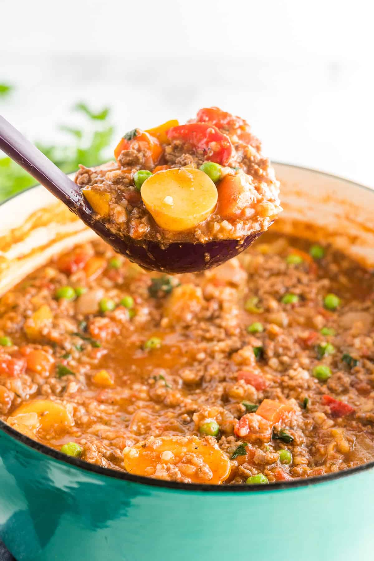 A close up a ladle full of stew being lifted from a pot.