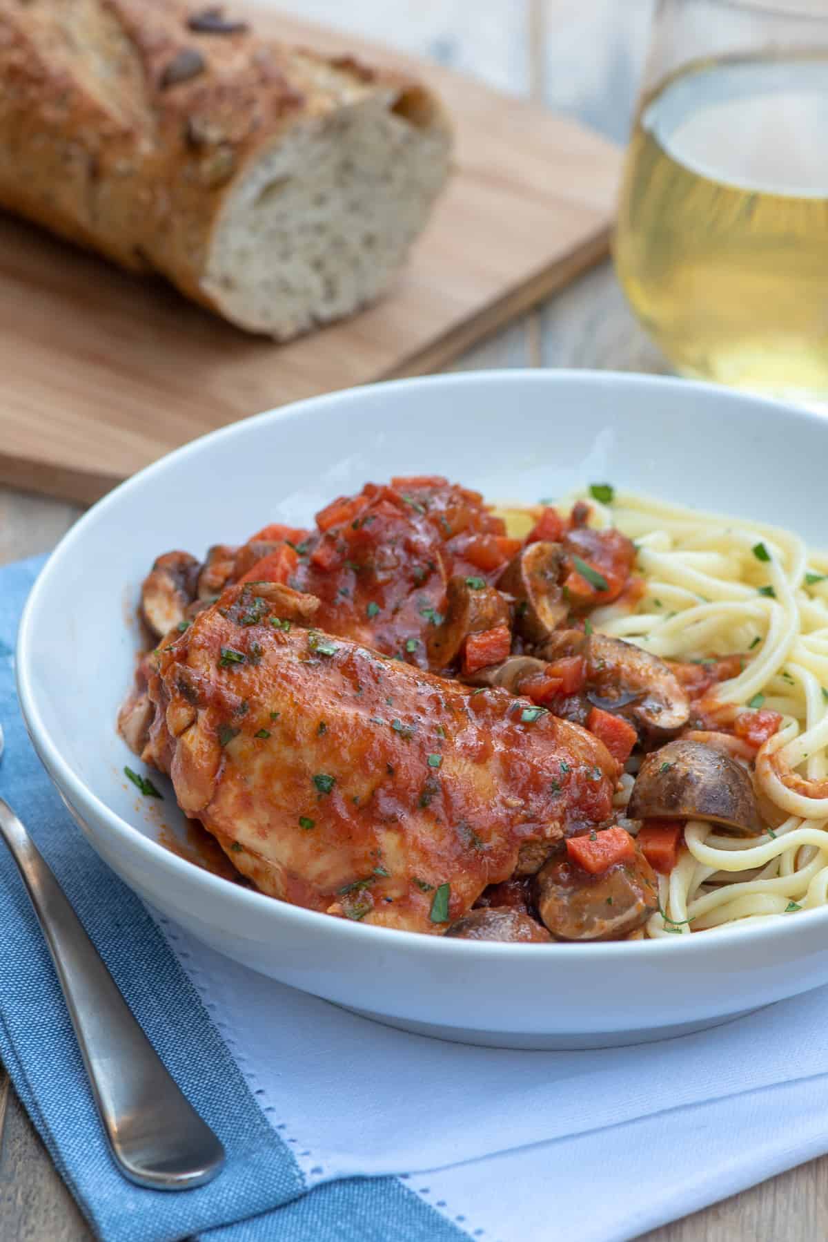 A serving of Slow Cooker Chicken Cacciatore in a white serving dish with pasta.