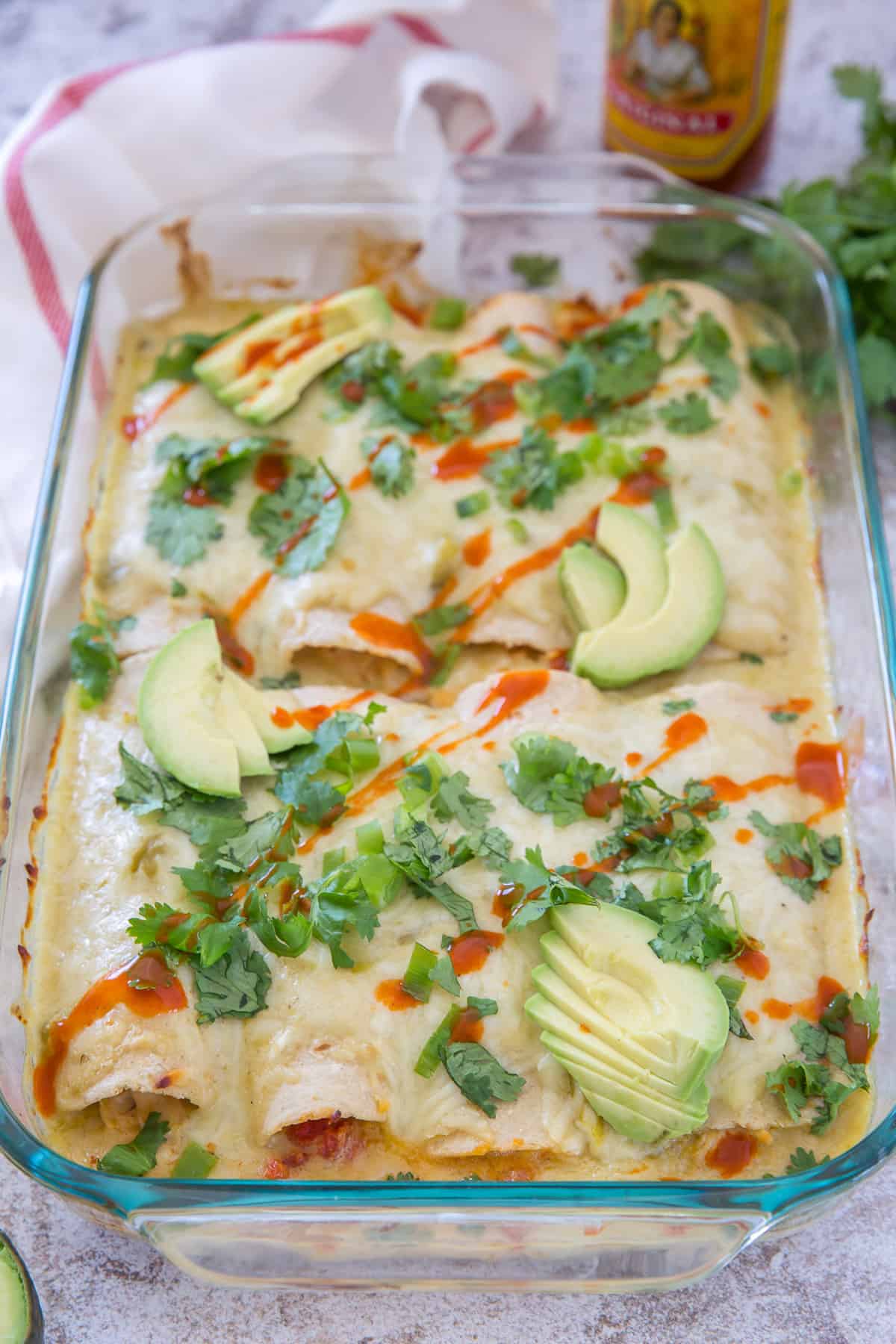 A casserole dish full of Sour Cream Chicken Enchiladas topped with cilantro, avocado and hot sauce.