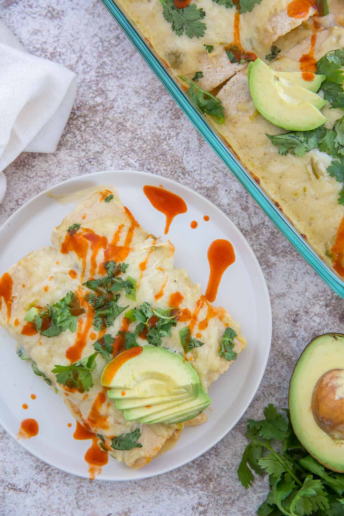 An over the top image of easy sour cream chicken enchiladas topped with cilantro, avocado and hot sauce.