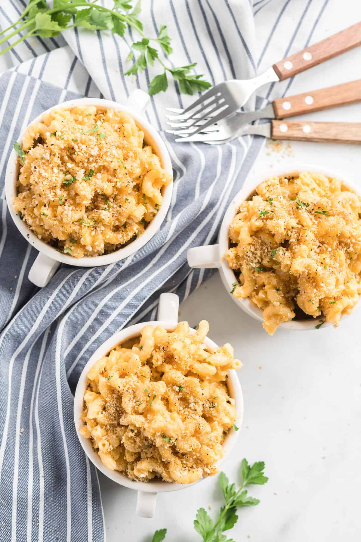 An over the top shot of three small serving bowls filled with Stovetop Macaroni and Cheese on a striped kitchen towel.