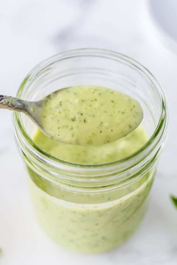 A spoon lifts some of the Basil Buttermilk Dressing from a mason jar.
