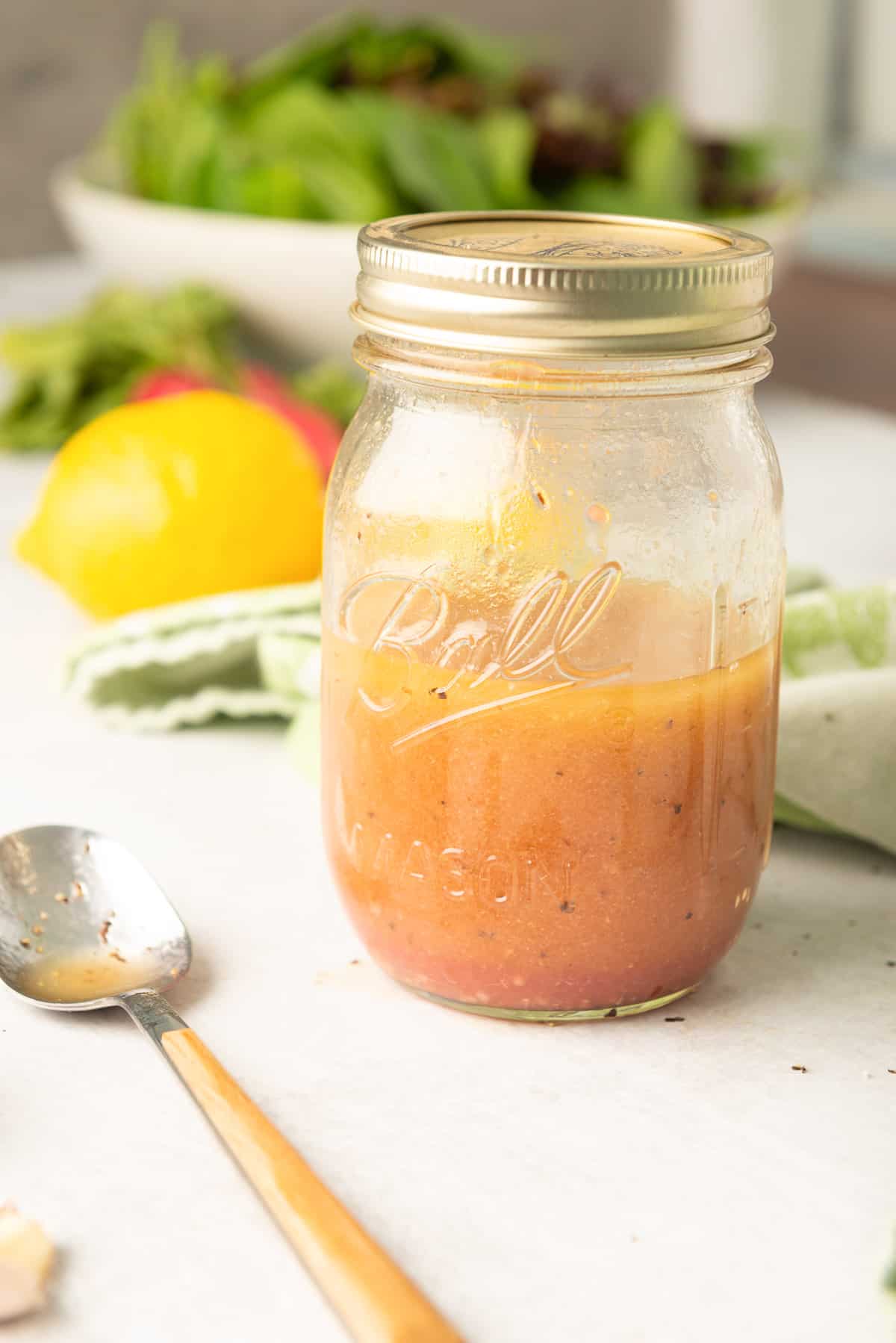 A mason jar filled with Cobb Salad Dressing with a spoon lying in front of it.