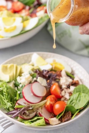 Dressing pours from a small glass bottle on to a bowl of salad.