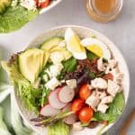 An over the top shot of Chicken Cobb Salad in a white bowl with a green and white cloth.