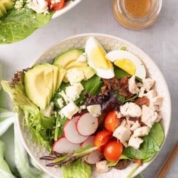 An over the top shot of Chicken Cobb Salad in a white bowl with a green and white cloth.