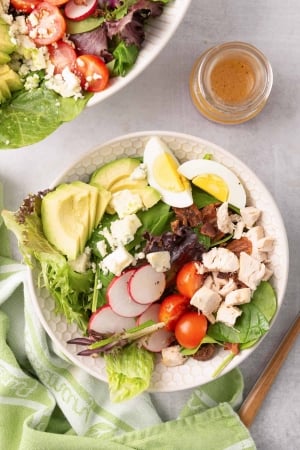 An over the top shot of Chicken Cobb Salad in a white bowl with a green and white cloth.