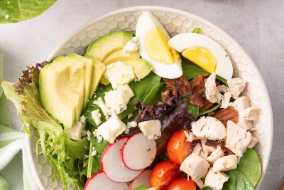 An over the top shot of Chicken Cobb Salad in a white bowl with a green and white cloth.